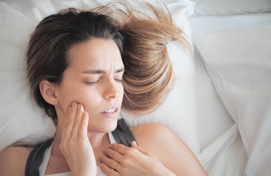 woman in bed with eyes closed and hand on jaw